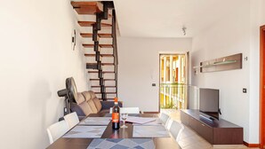 A modern living room with a dining area, a staircase, a TV, and a balcony. - Cadrezzate With Osmate (VA) (Osmate)