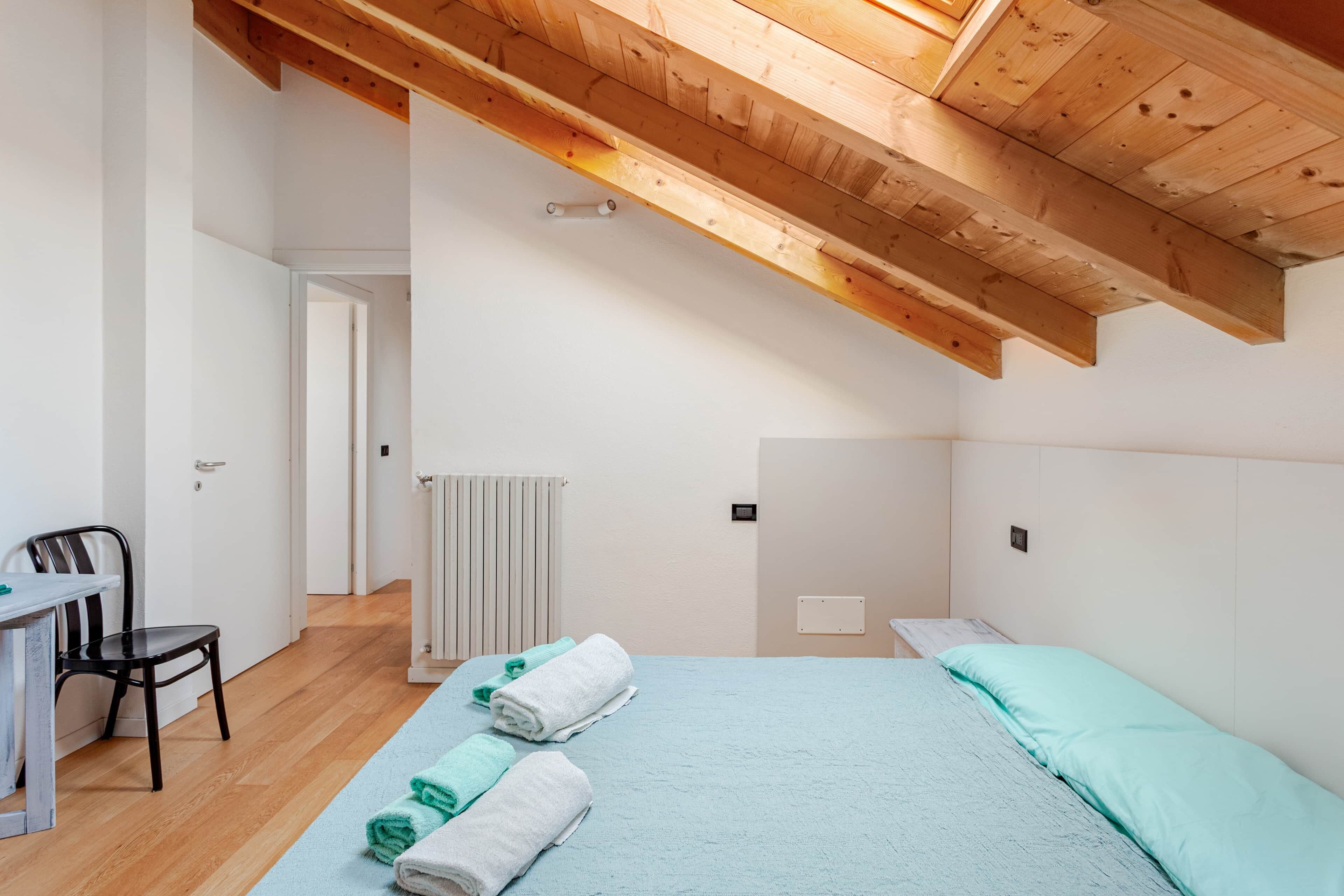 A bedroom with a sloped ceiling, a bed with light blue bedding, and a desk with a chair.
