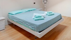 A bedroom with a sloped ceiling, skylights, a bed with a blue mattress and pillows, a white bedside table, and a white fan. - Cadrezzate With Osmate (VA) (Osmate)