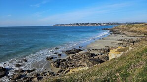 A coastal landscape with rocky cliffs, a sandy beach, and a clear blue sky.