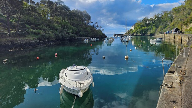 A calm river with boats docked, surrounded by lush greenery and a clear sky.