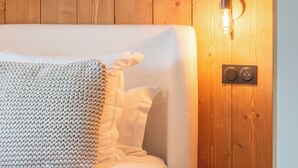 A wooden-paneled room with a bed, a small wooden stool, and a wall-mounted light fixture.