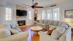 Una sala de estar con chimenea, televisor, ventilador de techo y un gran ventanal.