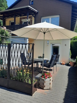 Eine Terrasse mit Tisch, Stühlen und einem großen Sonnenschirm, umgeben von einem Holzzaun.