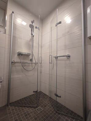 Une cabine de douche fermĂ©e par des parois en verre, Ă©quipĂ©e dâun pommeau de douche Ă main et dâun robinet mural.