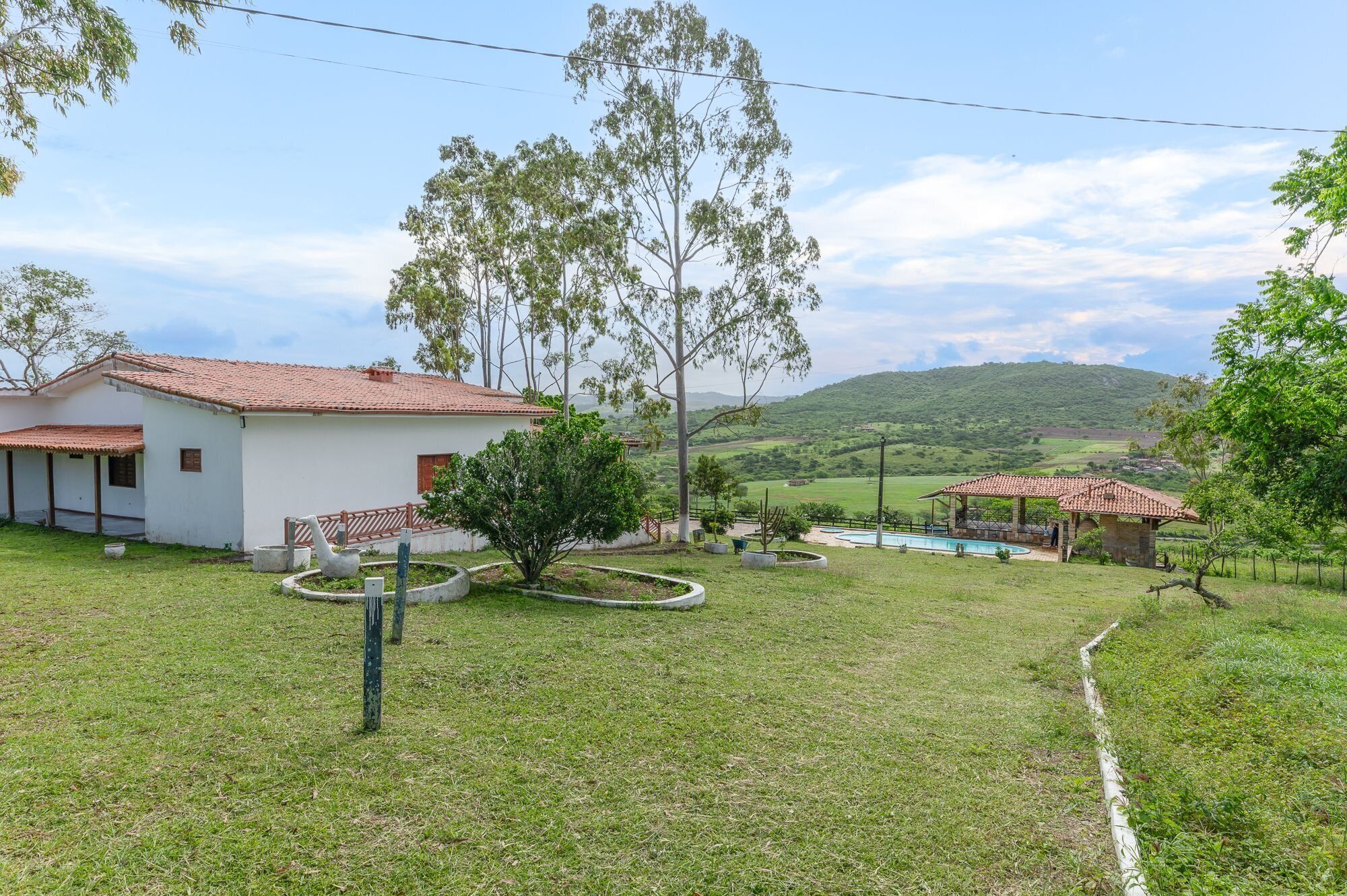 Ein Haus mit Ziegeldach, Schwimmbad und Blick auf grüne Hügel im Hintergrund.