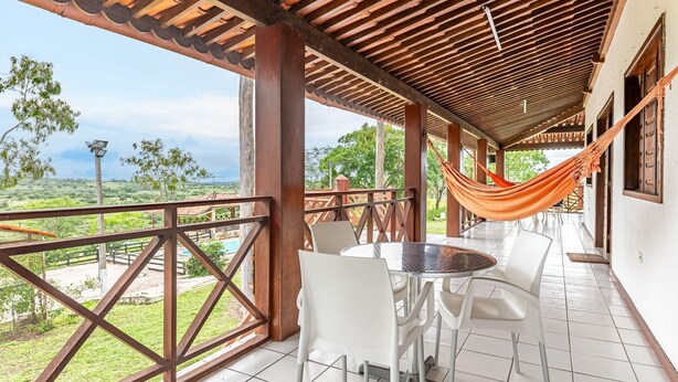 Un espacio al aire libre techado con una mesa y sillas, una hamaca y vistas a una piscina y follaje.