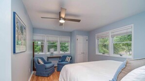 Une chambre à coucher avec un lit, deux chaises, un bureau et un ventilateur de plafond.