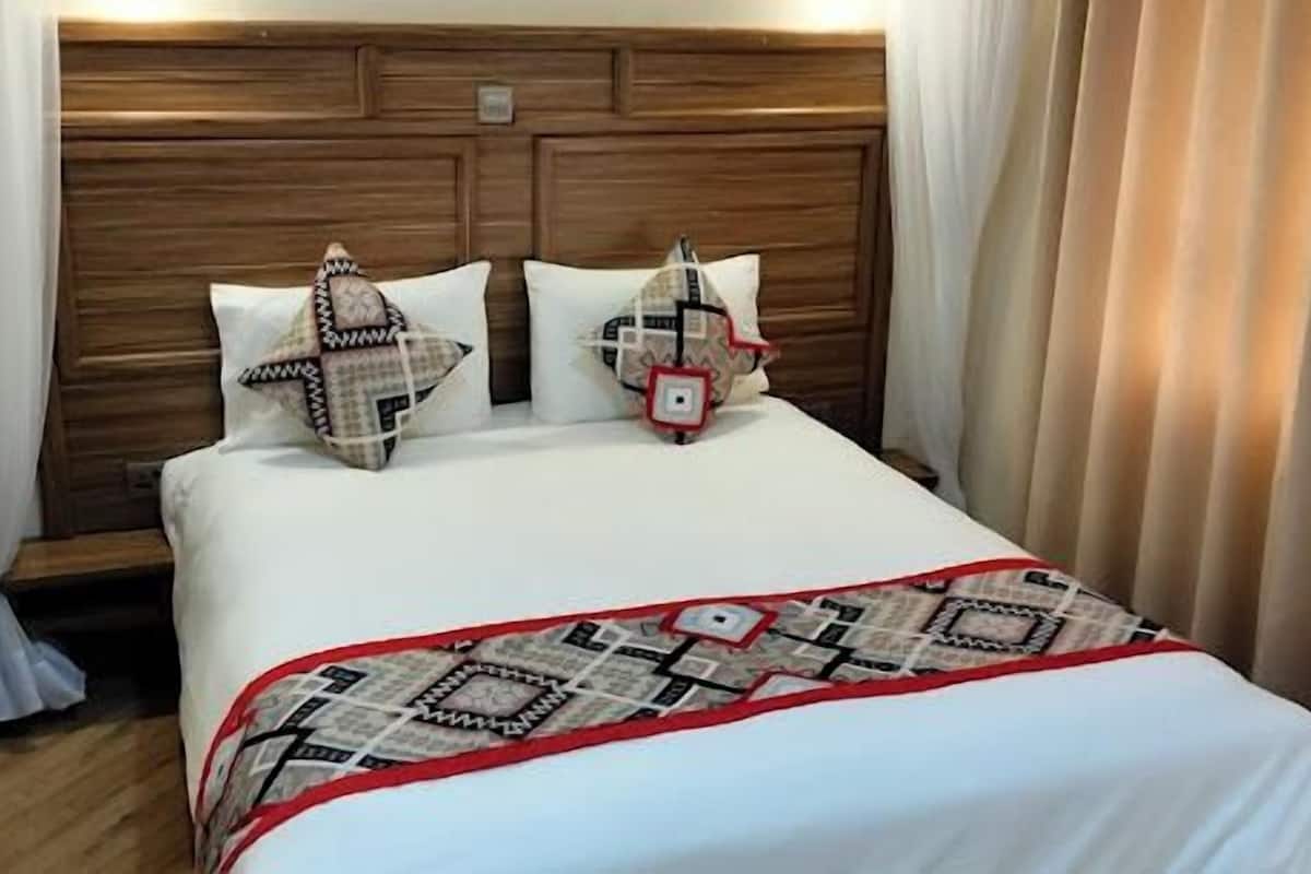 A neatly made bed with a patterned bedspread and pillows, a wooden headboard, and a bedside table with a lamp.