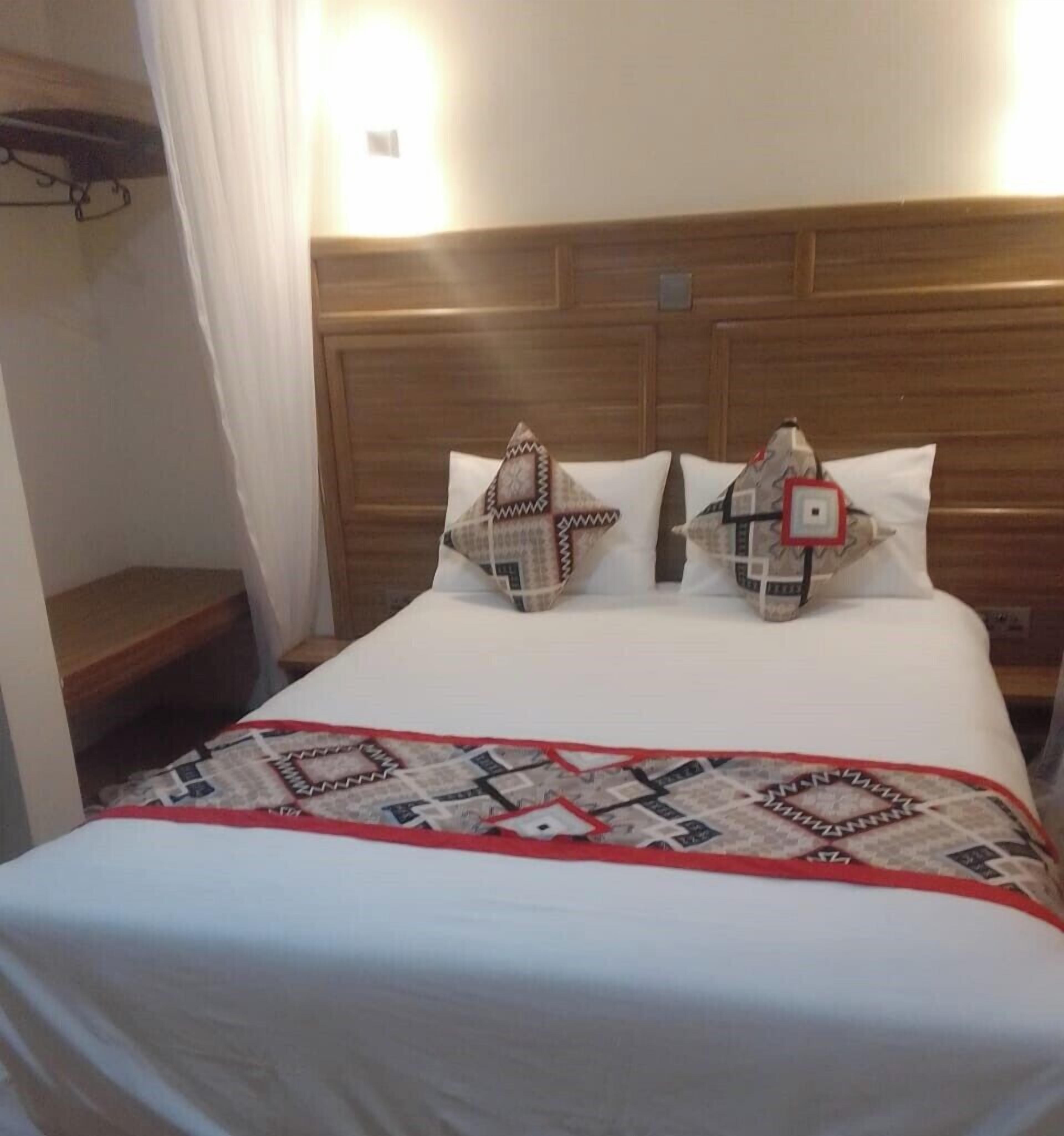 A neatly made bed with a patterned quilt and two pillows, a wooden headboard, and a bedside table with a lamp.