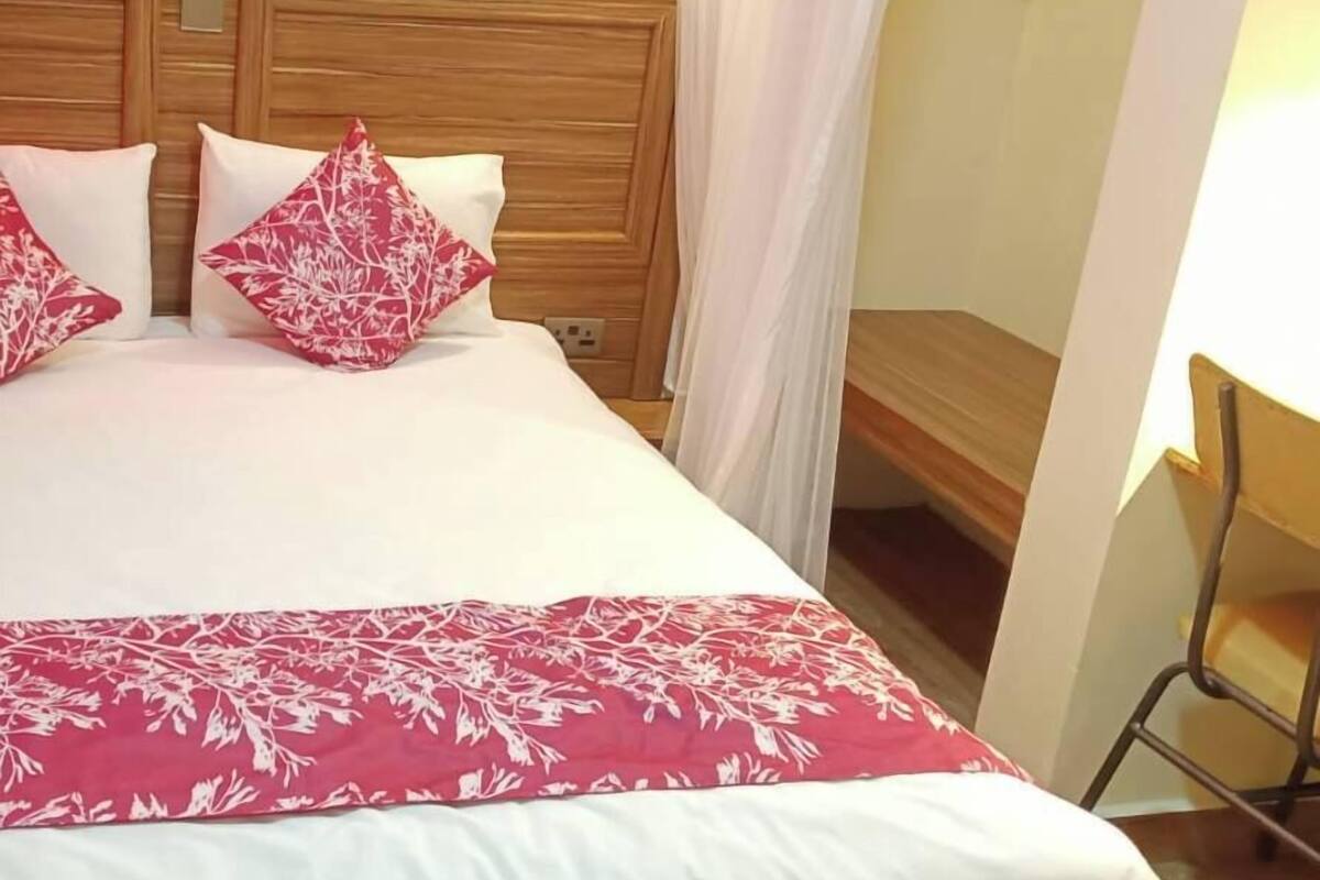 A hotel room with a wooden headboard, a bed with white and red floral bedding, and a small wooden bench.