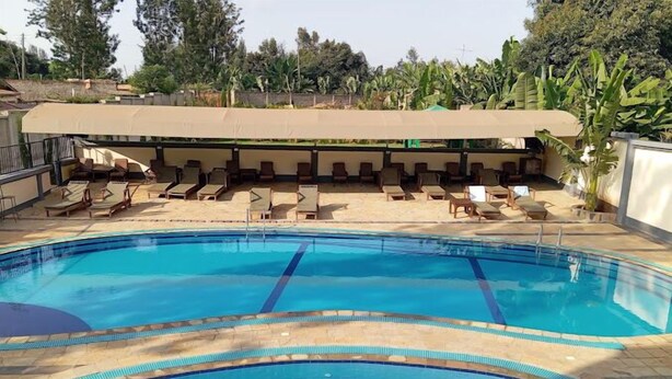 A swimming pool with lounge chairs and a covered seating area. - Sabby Grand Hotel (Thika)