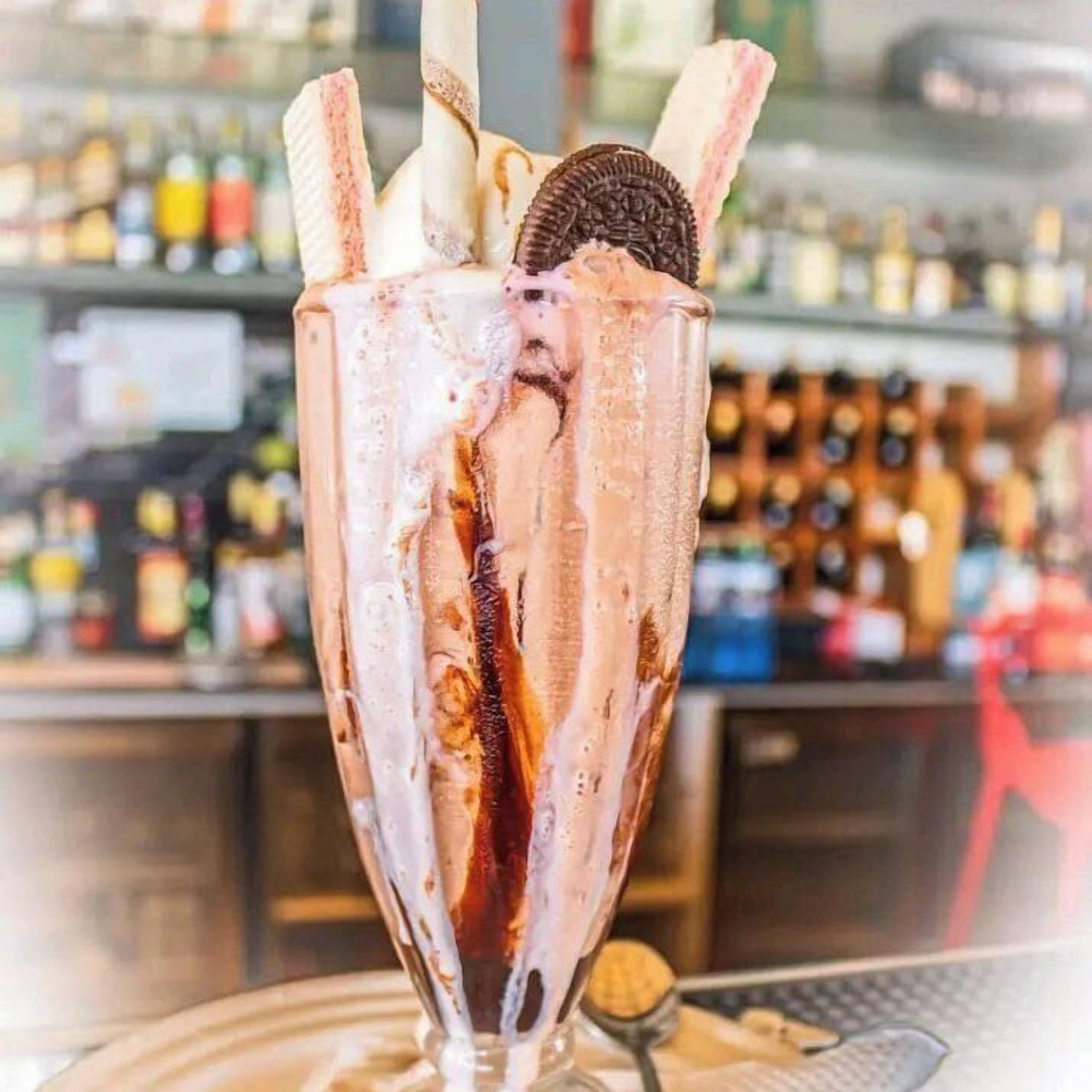 Um copo alto com uma bebida de chocolate, sorvete e um biscoito.