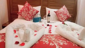 A neatly made bed with red and white floral pillows, a bottle of wine, and a blue box on the bed. - Sabby Grand Hotel (Thika)