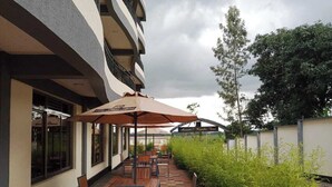 An outdoor seating area with tables and chairs, umbrellas, and a building facade with windows and a sign. - Sabby Grand Hotel (Thika)