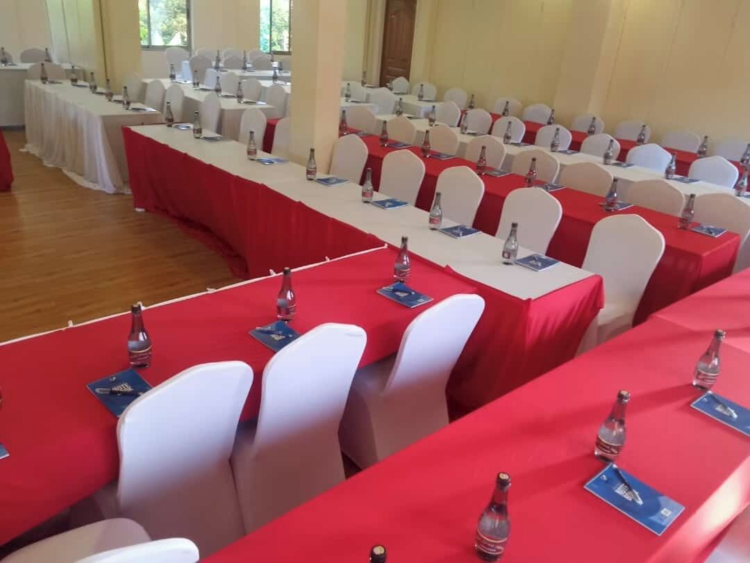 A conference room with rows of tables, each with white chairs and red tablecloths.