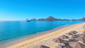 A beach with clear blue water, a yacht, and a row of beach umbrellas.