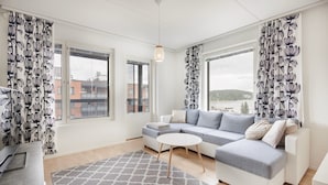 A modern living room with a grey sectional sofa, a small round coffee table, and a patterned rug. - Spacious 2BR Apt - Lake View & Sauna (Jyväskylä)