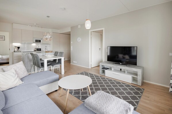 A modern living room with a grey sofa, a coffee table, and a TV on a white stand. - Spacious 2BR Apt - Lake View & Sauna (Jyväskylä)