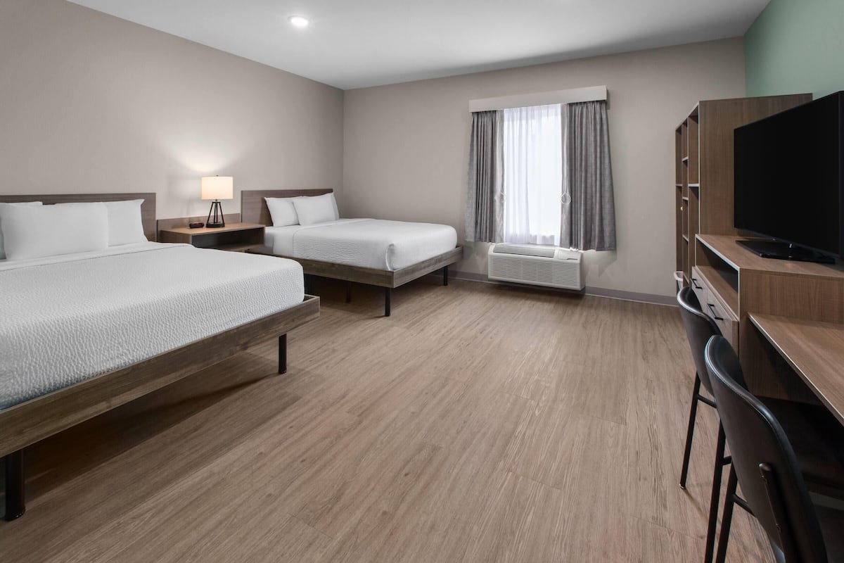Une chambre d’hôtel avec un grand lit, un plus petit lit, un bureau avec une télévision et une fenêtre avec des rideaux.