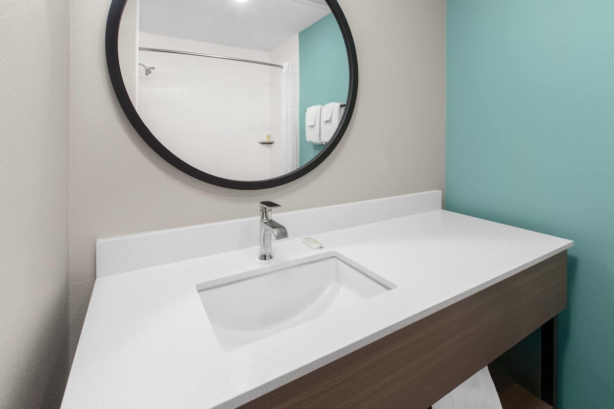 Une salle de bain avec un lavabo blanc, un miroir rond doté d’un cadre noir et un mur de couleur turquoise.