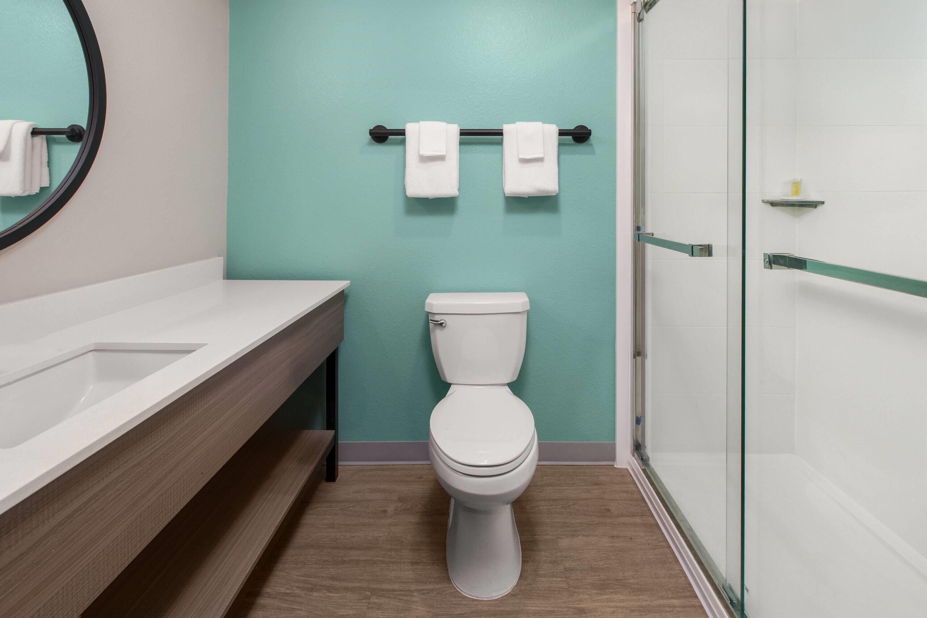 A bathroom with a toilet, a sink, a glass shower enclosure, and a towel rack with two towels.