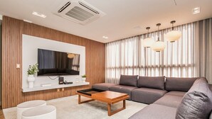 Una sala moderna con un sofá seccional, un televisor de pantalla plana, un muro decorativo de madera e iluminación colgante.