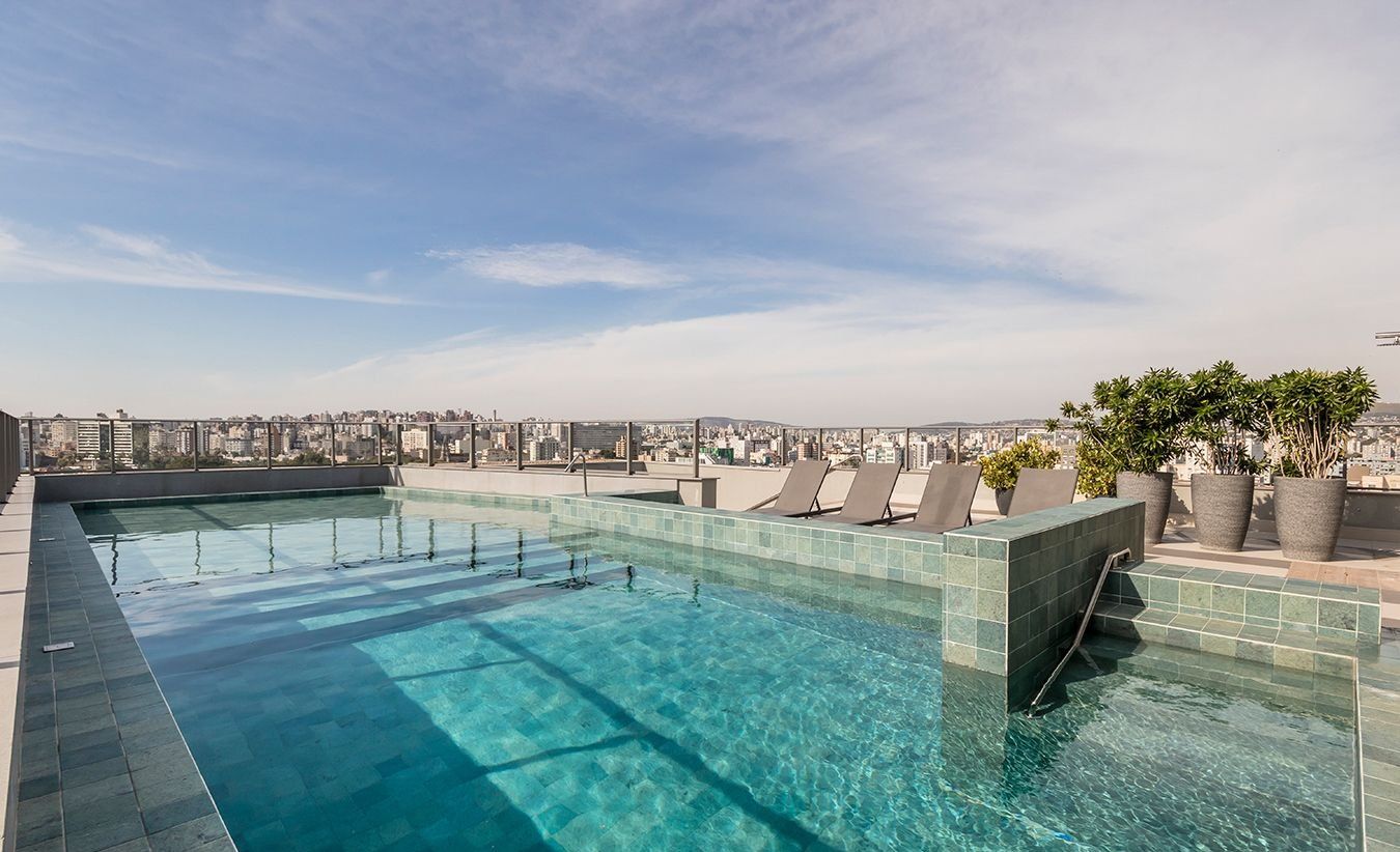Piscina infinita no terraço com vista para a cidade, espreguiçadeiras e plantas em vasos.