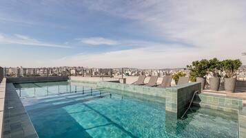 Piscina infinita no terraço com vista para a cidade, espreguiçadeiras e plantas em vasos.