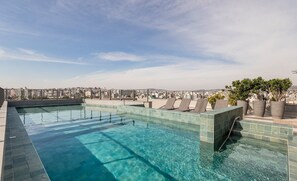 A rooftop infinity pool with a city view, lounge chairs, and potted plants. - Studio in Building With Swimming Pool in Porto Alegre - JRE (Porto Alegre)