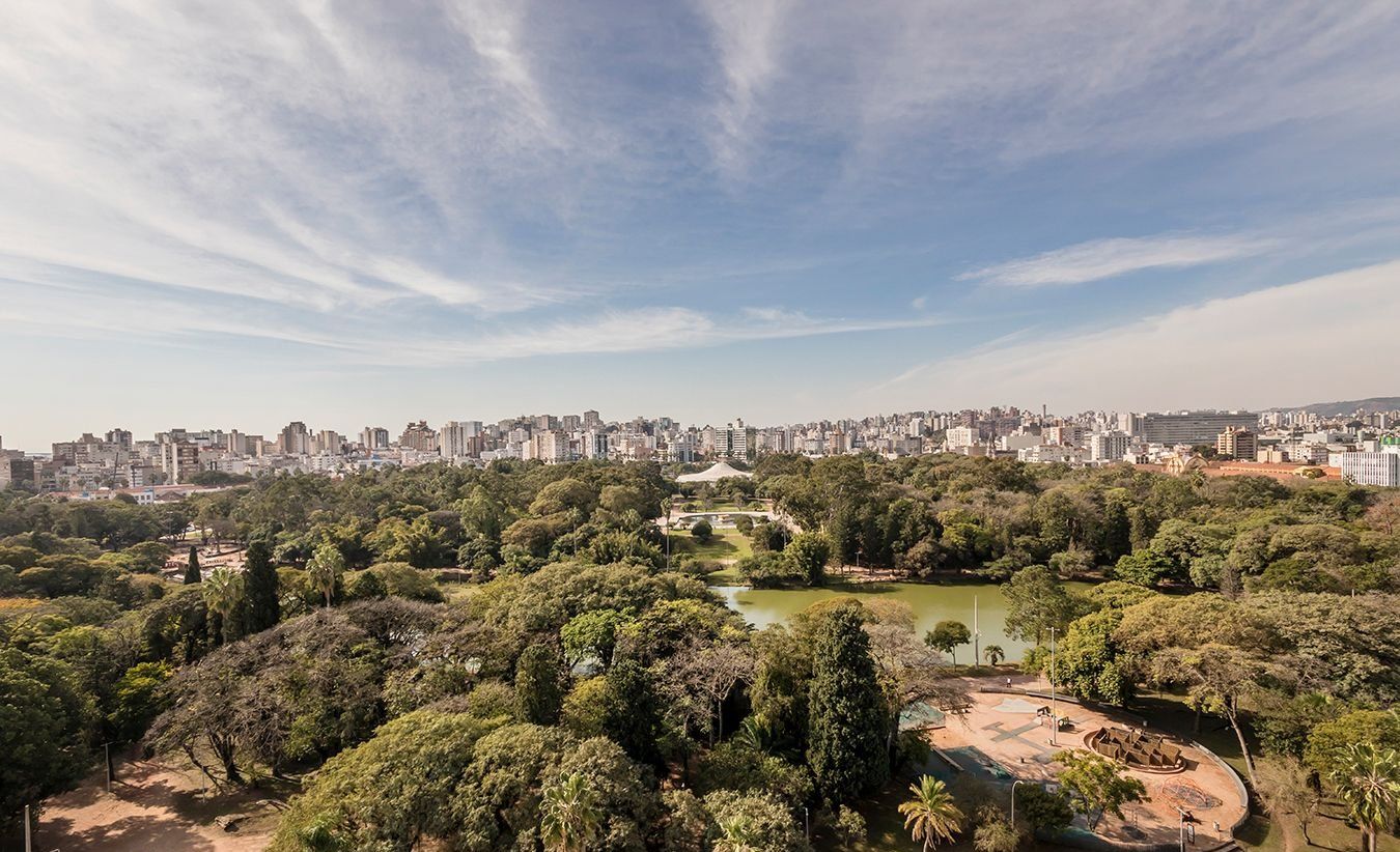 Un parc avec un lac, entouré d’une forêt dense, et en arrière-plan, le panorama de la ville.