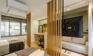 A modern hotel room with a sofa, a massage table, a TV mounted on the wall, and a desk with a chair. - Studio in Building With Swimming Pool in Porto Alegre - JRE (Porto Alegre)