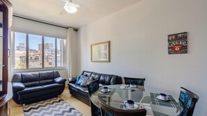 A living room with a glass table set for two, a black leather sofa, and a city view through large windows. - Comfortable ap 800 m From Redencao Park Eba0401 (Porto Alegre)