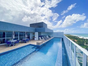 A rooftop pool with lounge chairs and tables, overlooking a beach and ocean. - Apto c Wi-fi Academia sal o de Jogos e Garagem (Salvador)