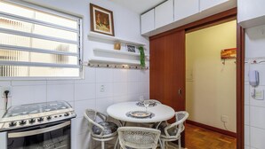 Una cucina compatta con piano cottura a gas, pareti rivestite di piastrelle bianche e un'area pranzo con sedie in vimini.