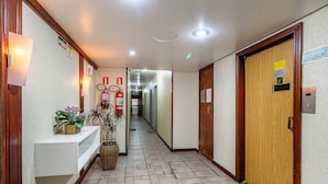 Un corridoio con una reception, piante in vaso, un estintore e una porta dell'ascensore.