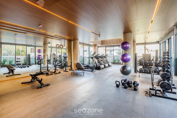 A spacious gym with various exercise equipment, large windows, and a modern design.