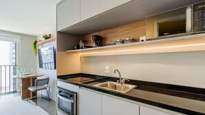 Una cocina moderna con horno empotrado, microondas y un lavamanos. Se ve un área de comedor con una mesa y sillas a través de una puerta abierta.
