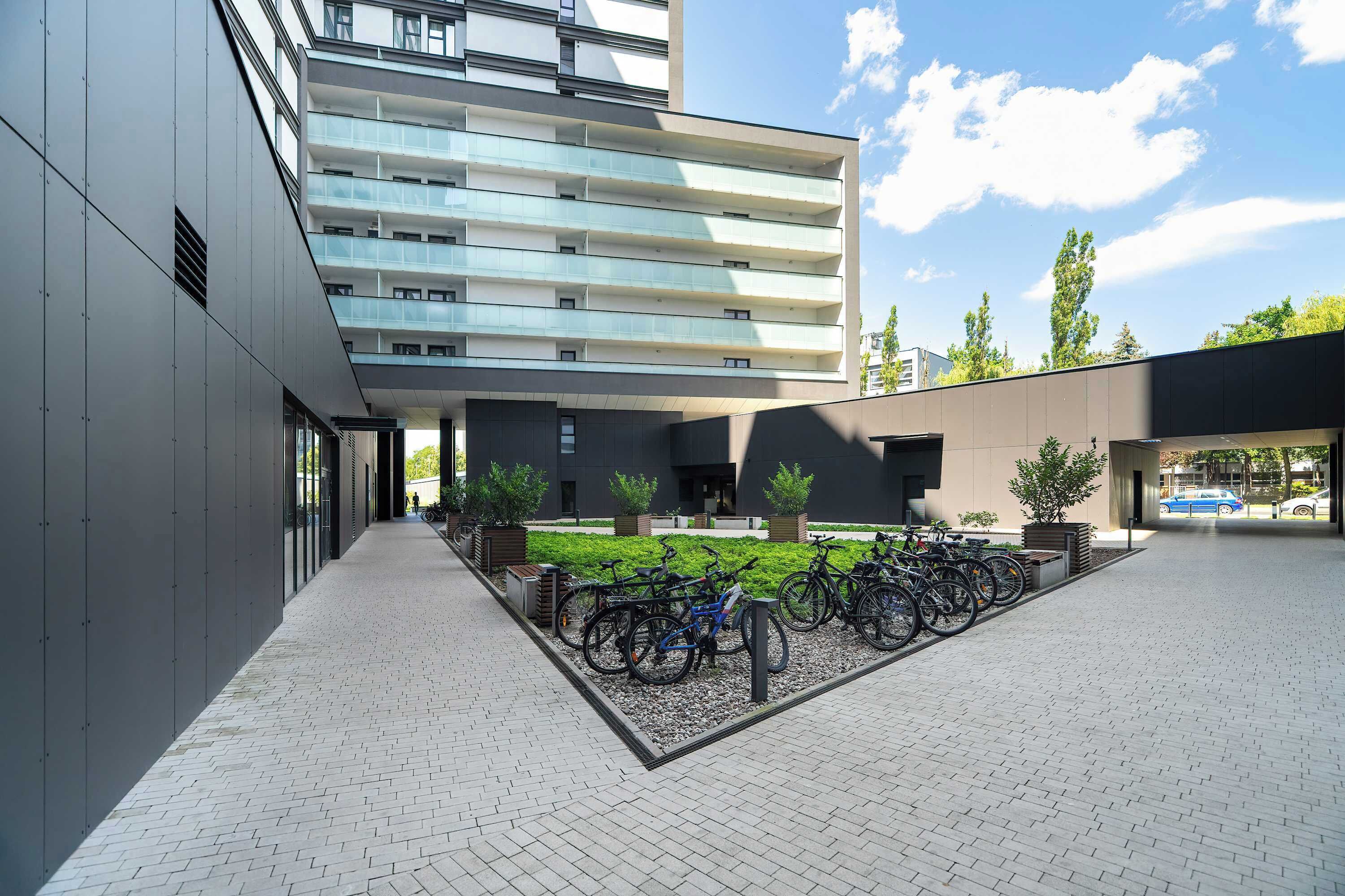 A modern building with multiple floors, a courtyard with bicycles, and a parking area.