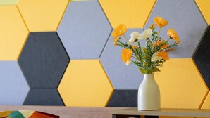 En vit vas med blommor står på ett träbord framför en vägg med geometriskt mönster.