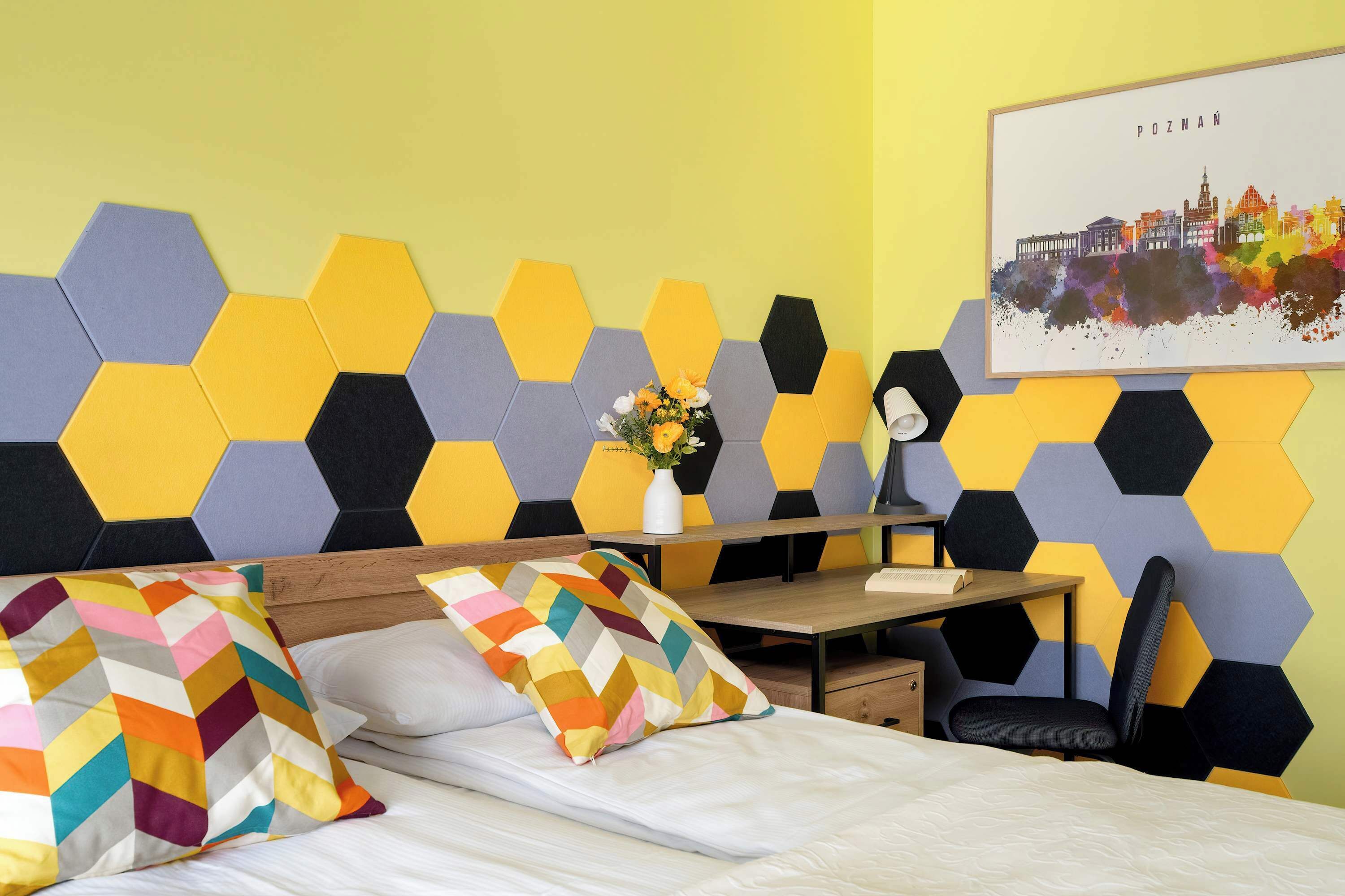 Ein Hotelzimmer mit Bett, Schreibtisch, Stuhl und einer Wand mit geometrischem Muster.