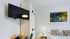 Un dormitorio moderno con cama, escritorio con computadora portátil, televisor montado en la pared y un cuadro en la pared.