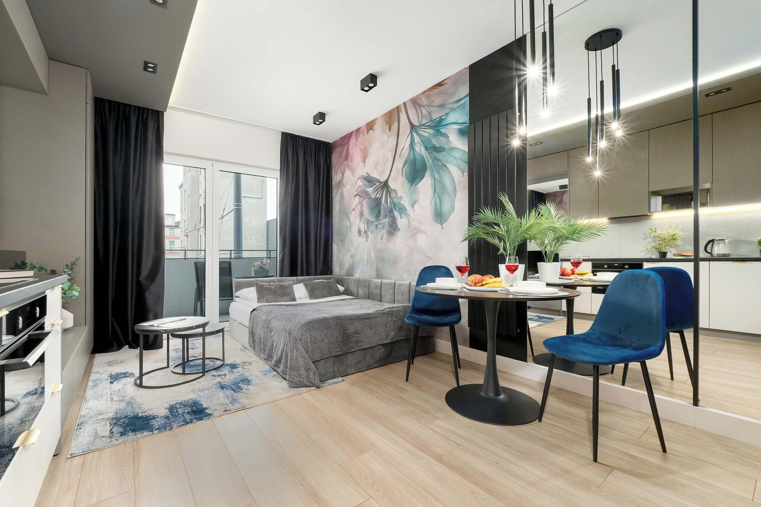 Een moderne woonkamer met een bank, een eettafel met stoelen, een keukenhoek en een groot raam met gordijnen.