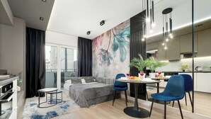 A modern living room with a sofa, a dining table with chairs, a kitchen area, and a large window with curtains.