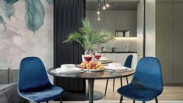 A modern dining area with a round table, two blue chairs, a potted plant, and a fruit bowl.