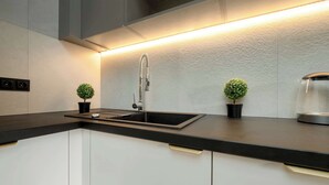 A modern kitchen with a black countertop, white cabinets, a stainless steel sink, and two small potted plants.