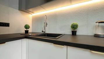 Una cucina moderna con piano di lavoro nero, mobili bianchi, lavello in acciaio inossidabile e due piccoli vasi con piante.