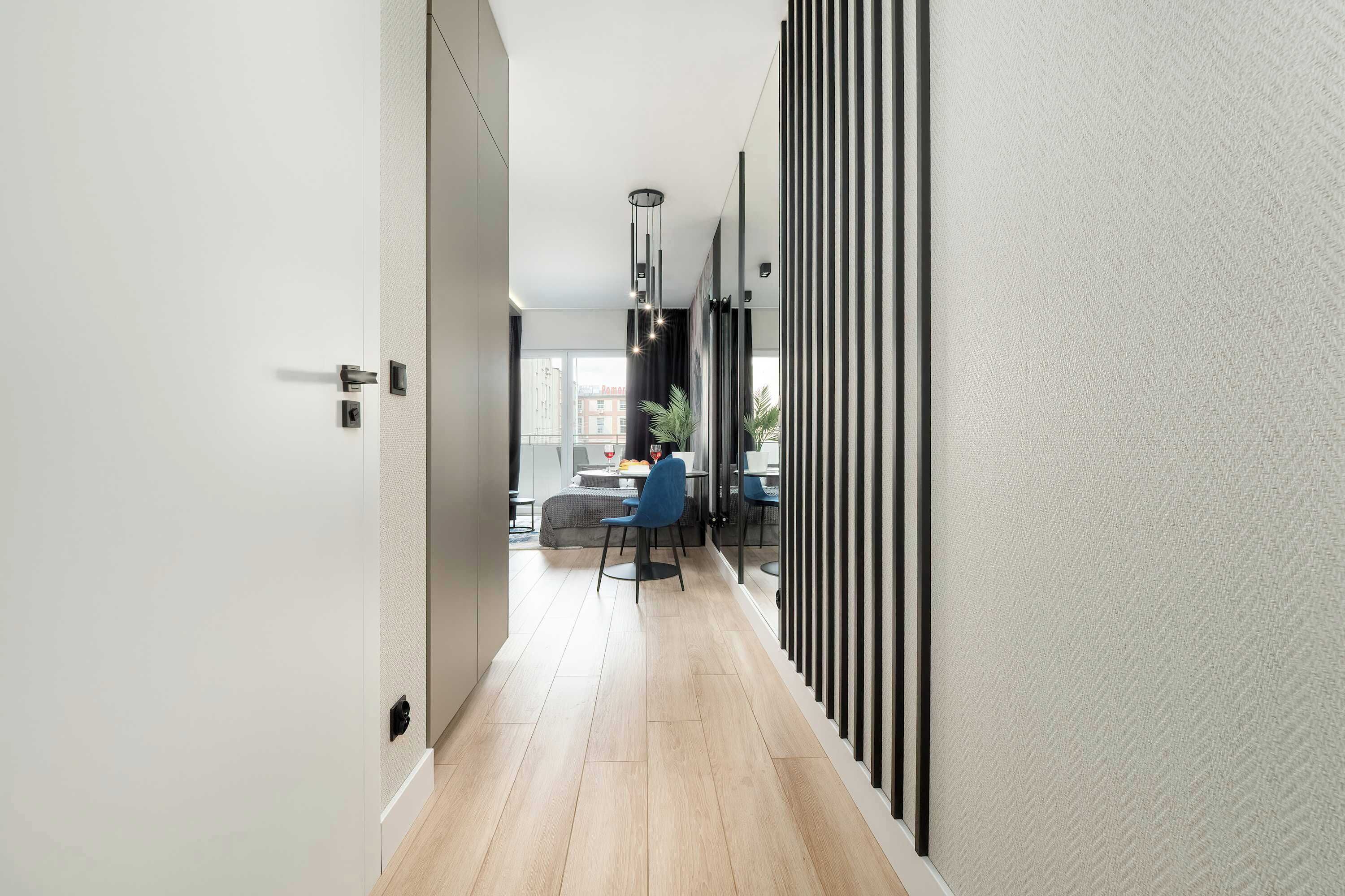 A modern hallway with a wooden floor, a dining area with a table and chairs, and a view of buildings outside.