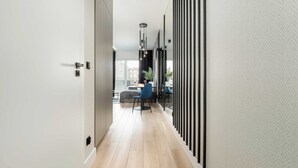 A modern hallway with a wooden floor, a dining area with a table and chairs, and a view of buildings outside.