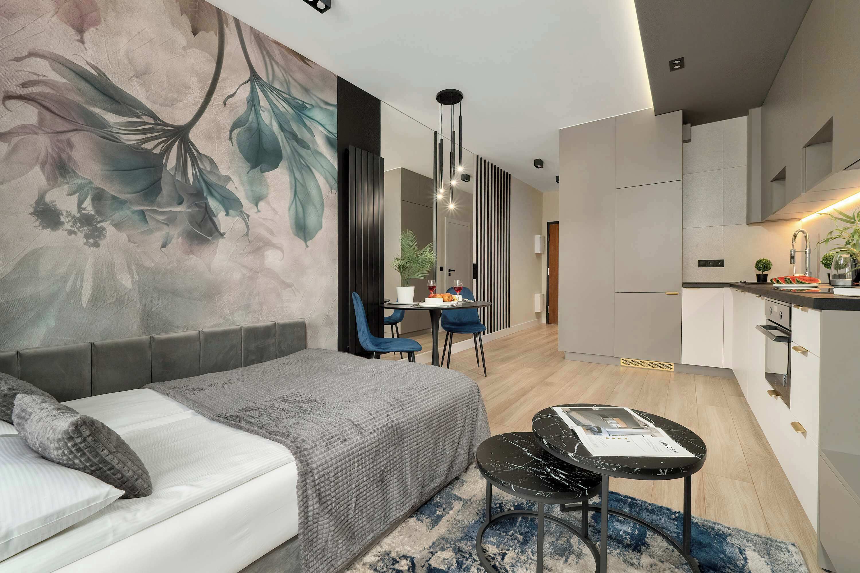 Een moderne hotelkamer met een bank, een eettafel met stoelen, een kitchenette en een grote bloemenmuur.